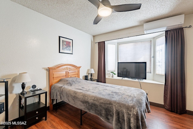 bedroom with baseboards, ceiling fan, wood finished floors, a wall mounted air conditioner, and a textured ceiling