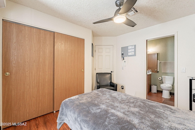 bedroom featuring a closet, visible vents, a textured ceiling, ensuite bath, and wood finished floors