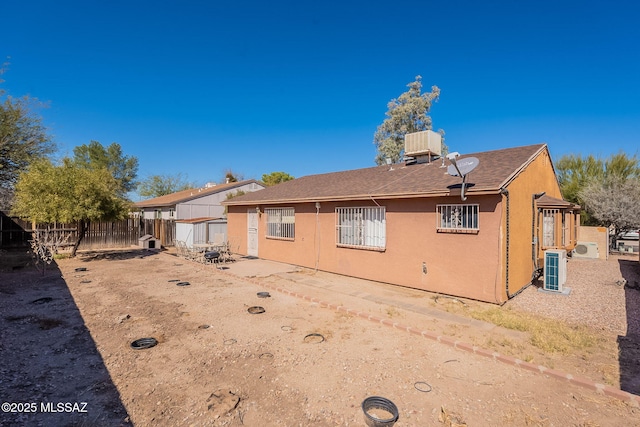 back of property with fence, central AC, and stucco siding