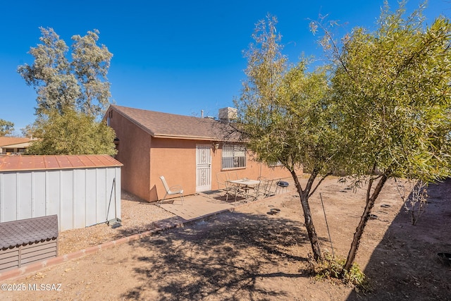 back of house featuring a patio, a shed, an outdoor structure, and stucco siding