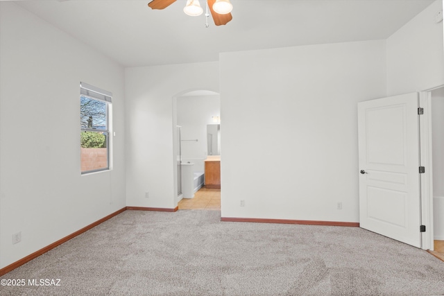 unfurnished bedroom featuring baseboards, arched walkways, light colored carpet, and ensuite bath