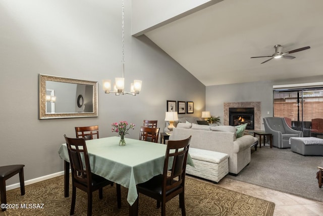 carpeted dining area featuring baseboards, a premium fireplace, high vaulted ceiling, tile patterned floors, and ceiling fan with notable chandelier