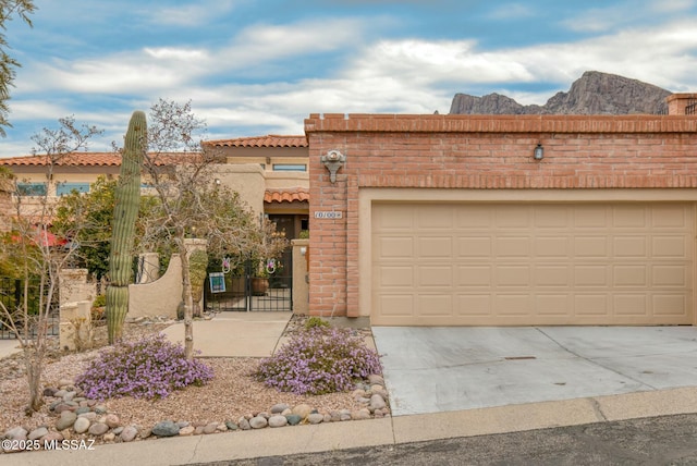 view of front of house with a gate, concrete driveway, an attached garage, brick siding, and a tiled roof