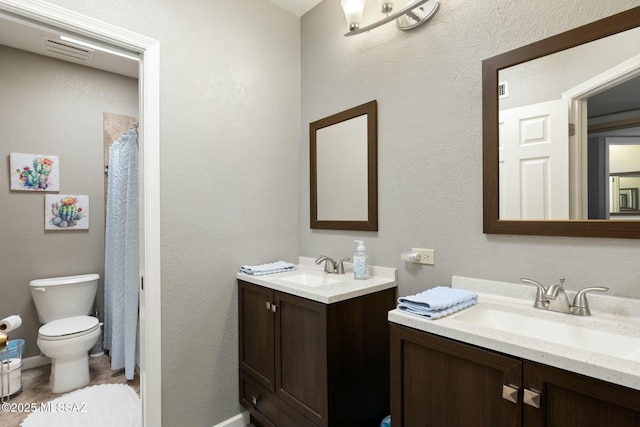 full bathroom featuring a sink, curtained shower, toilet, and two vanities