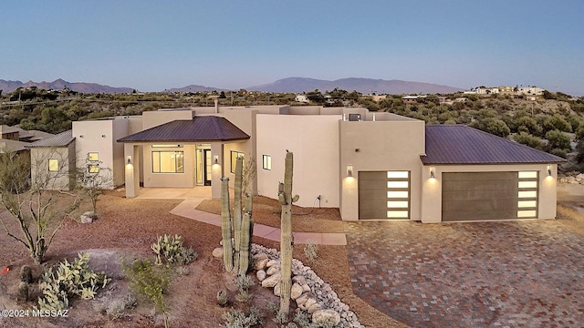 view of front facade with an attached garage, metal roof, decorative driveway, and stucco siding