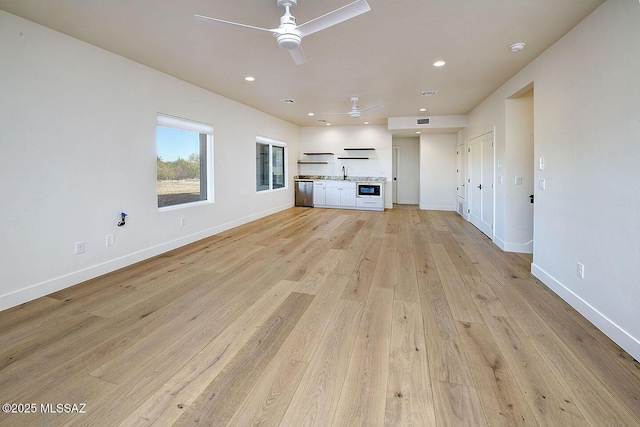 unfurnished living room featuring light wood finished floors, baseboards, ceiling fan, a sink, and recessed lighting