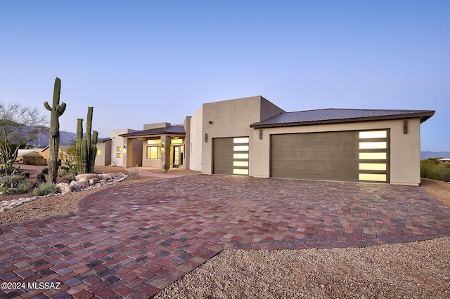 view of front of property with decorative driveway, metal roof, an attached garage, and stucco siding