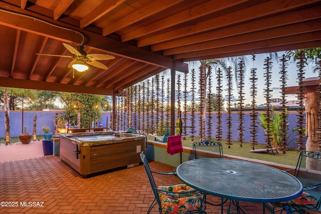 view of patio featuring outdoor dining space, a hot tub, a ceiling fan, and a water view