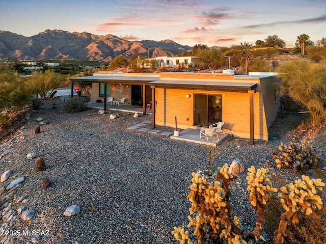 back of property at dusk featuring a patio, brick siding, and a mountain view