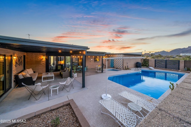 pool at dusk featuring a fenced in pool, fence, outdoor lounge area, a mountain view, and a patio