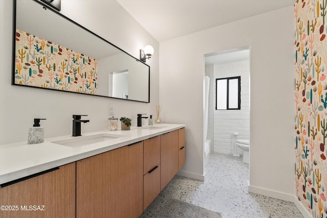 bathroom featuring double vanity, toilet, speckled floor, and a sink