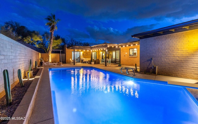 pool at night featuring an outdoor living space, a fenced backyard, a fenced in pool, and a patio