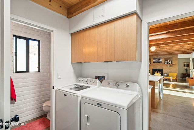 clothes washing area with wooden ceiling, cabinet space, separate washer and dryer, and a large fireplace