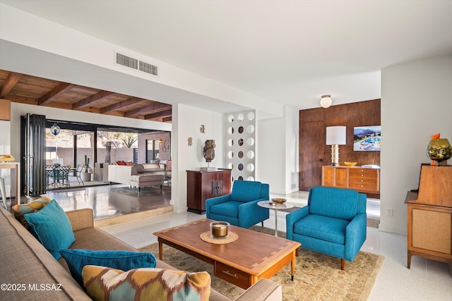 living area with beamed ceiling, visible vents, and wood walls