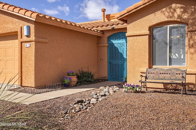 property entrance with an attached garage, a tile roof, and stucco siding