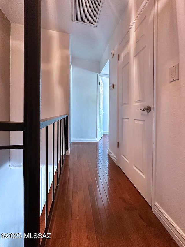 hallway with dark wood-type flooring, visible vents, and baseboards