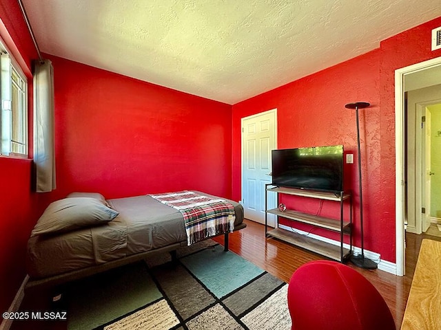 bedroom with a textured ceiling, a textured wall, wood finished floors, and baseboards