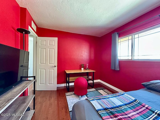 bedroom with a textured ceiling, wood finished floors, visible vents, and baseboards