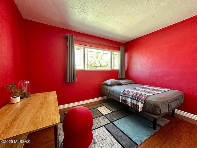 bedroom featuring a textured ceiling, baseboards, wood finished floors, and a textured wall