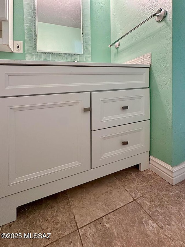 bathroom featuring baseboards, a textured wall, vanity, and a textured ceiling