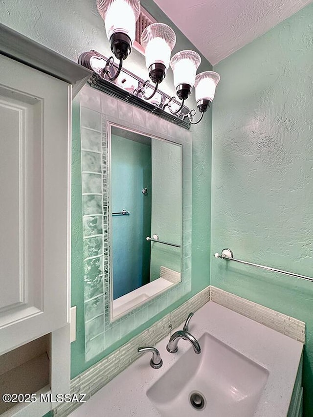 bathroom with a textured ceiling, a textured wall, a sink, and a notable chandelier