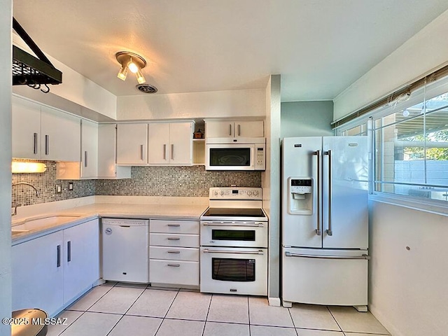 kitchen featuring light tile patterned floors, light countertops, decorative backsplash, a sink, and white appliances