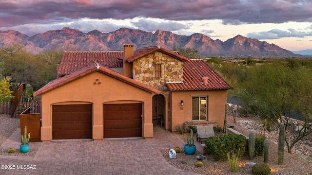 mediterranean / spanish-style house with an attached garage, stucco siding, decorative driveway, and a tiled roof