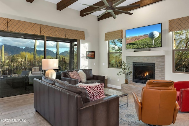 living room featuring beam ceiling, light wood finished floors, a ceiling fan, a mountain view, and a warm lit fireplace