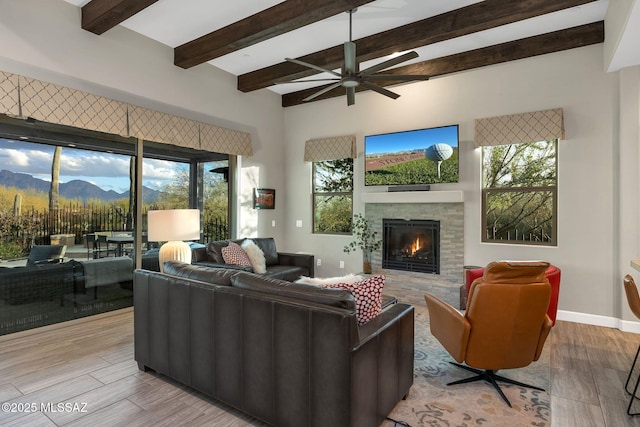 living area with a ceiling fan, light wood-style floors, baseboards, beamed ceiling, and a glass covered fireplace