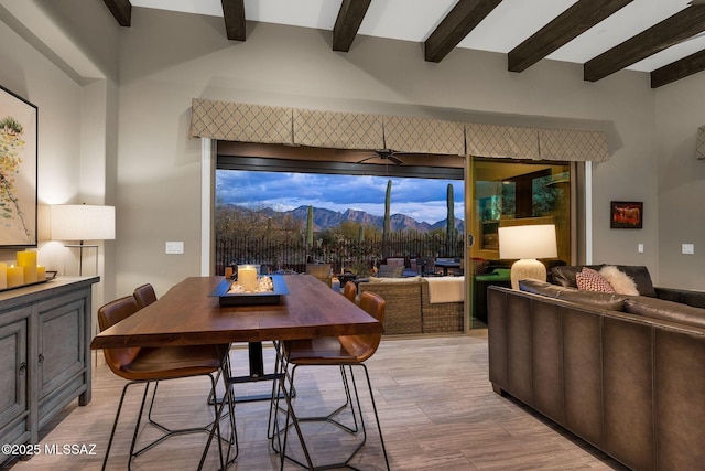 dining area featuring light wood-style flooring, beamed ceiling, a mountain view, and a ceiling fan