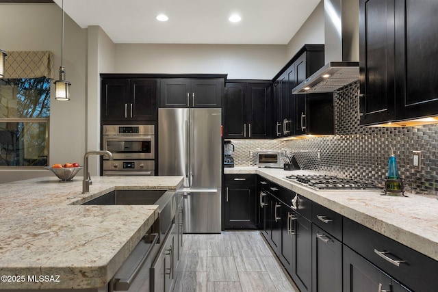 kitchen with tasteful backsplash, appliances with stainless steel finishes, dark cabinets, wall chimney range hood, and pendant lighting