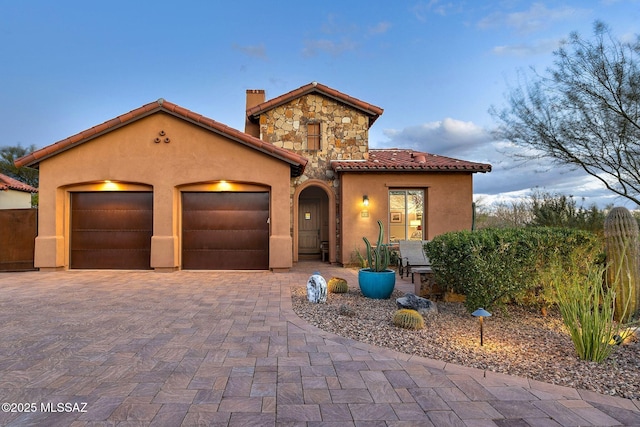 mediterranean / spanish-style house featuring stone siding, decorative driveway, an attached garage, and stucco siding