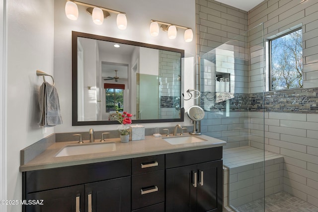 full bath featuring double vanity, tiled shower, a sink, and a ceiling fan