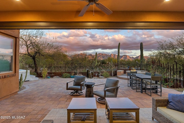 patio terrace at dusk featuring outdoor dining area, a mountain view, an outdoor hangout area, fence, and a ceiling fan