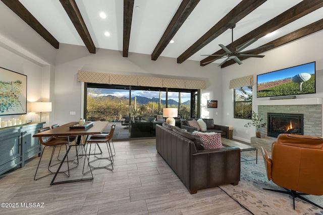 living area featuring a ceiling fan, beam ceiling, and a glass covered fireplace