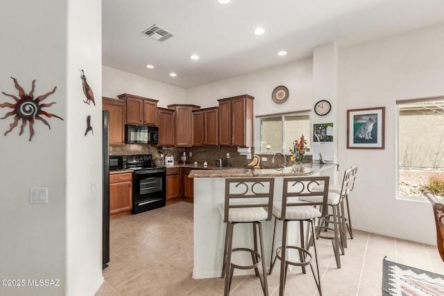 kitchen featuring visible vents, decorative backsplash, a breakfast bar, a peninsula, and black appliances