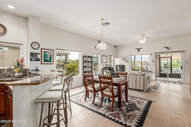 dining space with light tile patterned floors, a fireplace, visible vents, and ceiling fan with notable chandelier