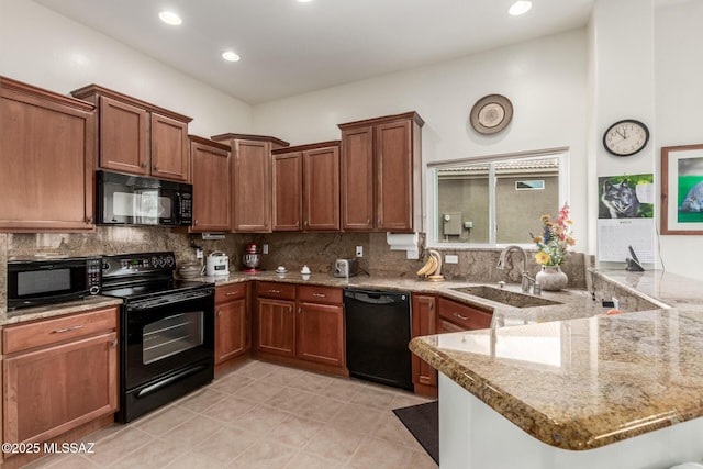 kitchen with light stone counters, a peninsula, a sink, black appliances, and backsplash