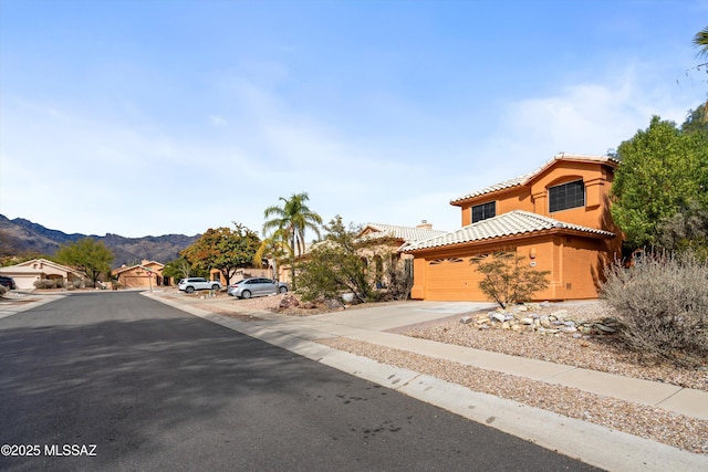 view of front of home featuring a tile roof, stucco siding, an attached garage, a mountain view, and driveway