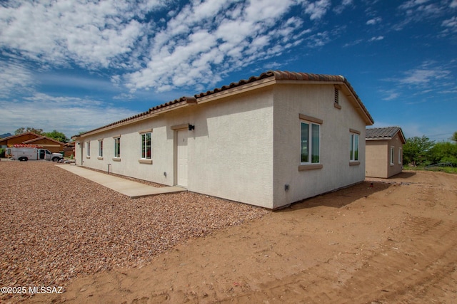 back of house featuring a tiled roof and stucco siding