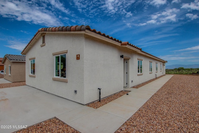 view of side of property featuring a tile roof, a patio area, and stucco siding