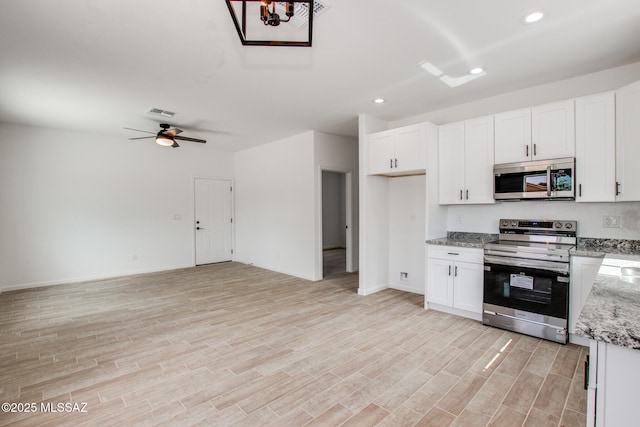 kitchen featuring appliances with stainless steel finishes, open floor plan, light stone counters, light wood-style floors, and white cabinetry