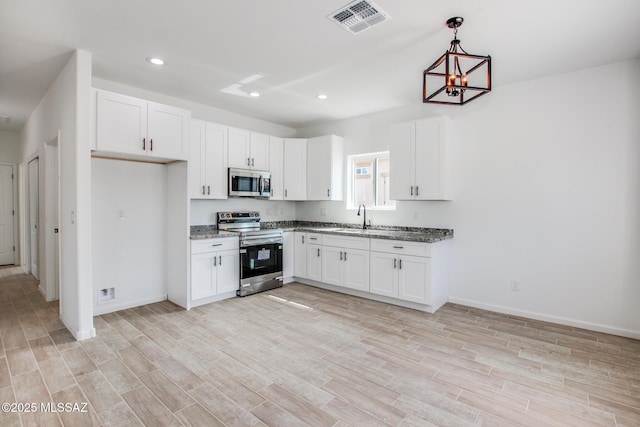 kitchen with appliances with stainless steel finishes, white cabinets, visible vents, and light wood-style floors