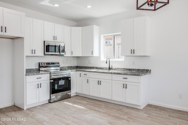 kitchen featuring appliances with stainless steel finishes, white cabinets, a sink, and wood finish floors