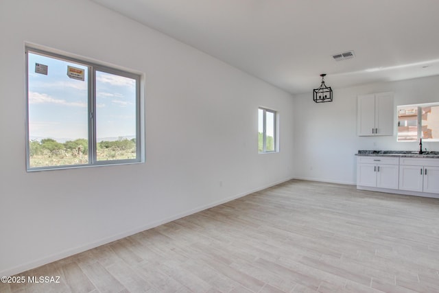 interior space featuring light wood-type flooring, visible vents, a sink, and baseboards