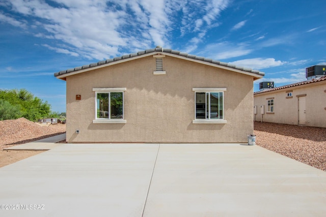 rear view of house featuring a tile roof, central air condition unit, a patio area, and stucco siding