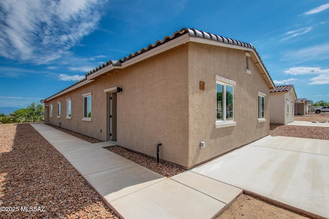 view of side of home featuring a patio area, a tiled roof, and stucco siding