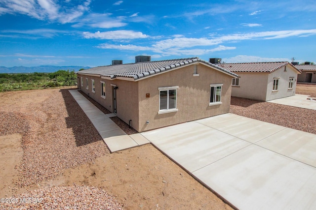 view of front of house with a patio area, a tile roof, central AC, and stucco siding