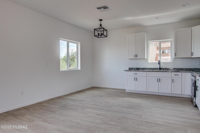 kitchen featuring a sink, white cabinetry, baseboards, visible vents, and light wood-style floors