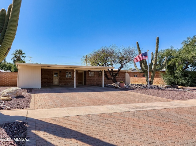 view of front facade with a carport, decorative driveway, brick siding, and fence